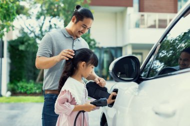 Progressive father and daughter returned from school in electric vehicle that is being charged at home. Electric vehicle driven by renewable clean energy. Home charging station concept for environment
