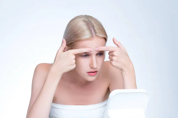 Acne problem troubling personable worried woman with natural beauty skin checking her face squeezing pimple spots in isolated background. Copyspace for blemish skincare treatment problem.