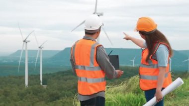 Erkek ve kadın mühendisler kırsal kesimdeki bir tepenin tepesinde ya da dağda rüzgar çiftliğinde çalışıyorlar. Yenilenebilir ve sürdürülebilir enerjinin gelecekteki üretimi için yenilikçi idealler.