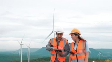 Erkek ve kadın mühendisler kırsal kesimdeki bir tepenin tepesinde ya da dağda rüzgar çiftliğinde çalışıyorlar. Yenilenebilir ve sürdürülebilir enerjinin gelecekteki üretimi için yenilikçi idealler.