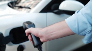 İlerici işadamı, şehir merkezinde dolaşmadan önce şarj cihazından elektrikli arabasına şarj prizi takıyor. Çevre dostu şarj edilebilir araba, sürdürülebilir ve temiz enerjiyle çalışıyor..