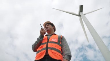 Gökyüzü arka planına sahip bir rüzgar türbini üzerinde çalışan mühendis. Yenilenebilir ve sürdürülebilir enerjinin gelecekteki üretimi için yenilikçi bir ideal. Rüzgar türbininden enerji üretimi.