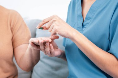 Contented senior woman sit along side with her husband, taking medicines while her caregiver advising her medication. Medication for seniors, nursing house, healthcare at home.