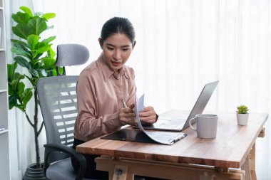 Modern ofis masasındaki Asyalı hevesli genç iş kadını çalışmak ve notlar yazmak için dizüstü bilgisayar kullanıyor. Çalışkan ve çekici ofis hanımı ofisinde bilgisayar defteri üzerinde çalışıyor..