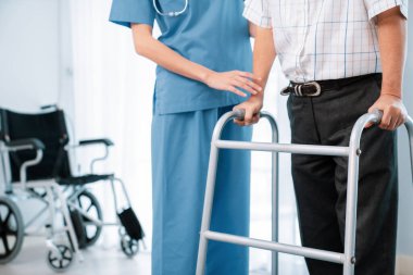 Physiotherapist assists her contented senior patient on folding walker. Recuperation for elderly, seniors care, nursing home.