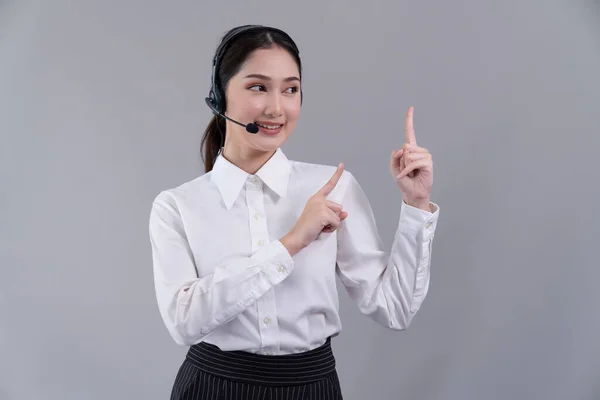 亚洲女性呼叫中心操作员面带微笑地刊登招聘广告 穿着正式西服 头戴耳机 在可定制的隔离背景下对产品指指指点点 很有激情 — 图库照片