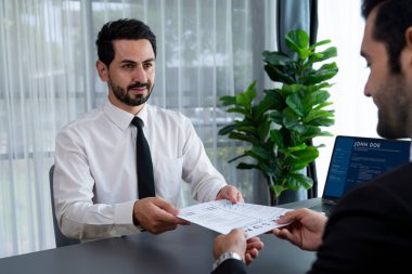 Resmi ofiste takım elbise giyen kendine güvenen bir adam, iş görüşmesi sırasında özgeçmiş kağıtlarını tutuyor. Sorular soran, aday yeterliliği ve iş için uygunluk değerlendirmesi yapan bir muhabir. Coşkulu