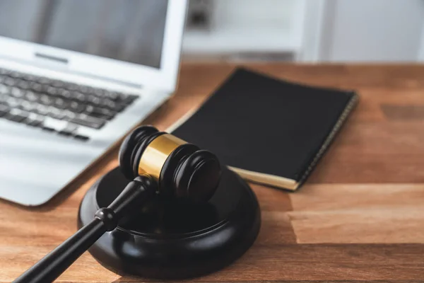 弁護士や裁判官のための司法制度として木製のオフィステーブルの背景にノートパソコンや本や机の上にペンで木製のギャベルハンマーを閉じます 裁判で権威と公平性を象徴します 公平性 — ストック写真