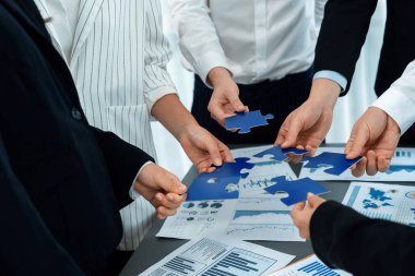 Closeup top view business team of office worker putting jigsaw puzzle together over table filled with financial report paper in workplace with manager to promote harmony concept in meeting room.