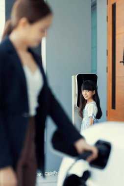 Evde şarj edilen elektrikli bir araçla okuldan yeni dönen anne ve kızın ilerici yaşam tarzı. Elektrikli araç, sürdürülebilir temiz enerjiyle çalışıyor..