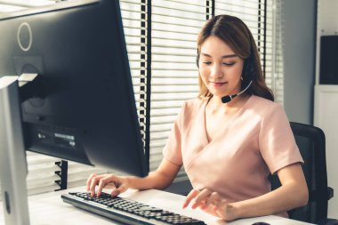 Competent female operator working on computer and while talking with clients. Concept relevant to both call centers and customer service offices.