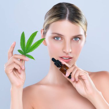 Alluring portrait of beautiful woman in isolated holding green leaf with marijuan extracted bottle for skincare treatment product. Cannabis CBD oil for cosmetology and beauty concept.