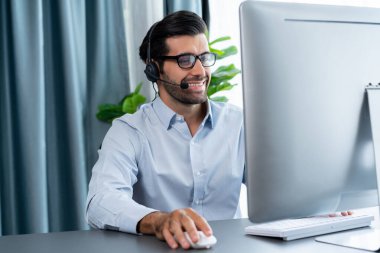 Erkek çağrı merkezi operatörü ya da telesales temsilcisi ofis masasında oturmuş kulaklık takıyor ve müşteri hizmetleri desteği sağlayan ya da satış yapan müşteriyle sohbet ediyor. coşkulu