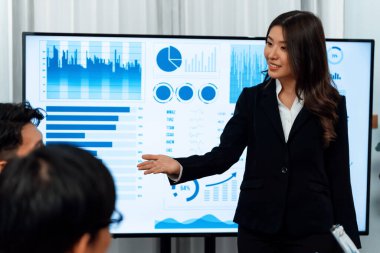 Confidence and young asian businesswoman give presentation on financial business strategy in dashboard report display on screen to colleagues in conference room meeting as harmony in workplace concept