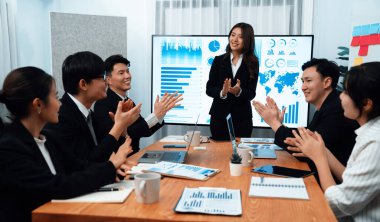 Confidence and young asian businesswoman give presentation on financial business strategy in dashboard report display on screen to colleagues in conference room meeting as harmony in workplace concept