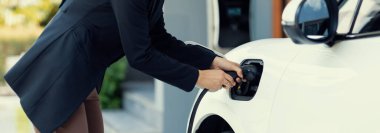 İlerici kadın elektrikli arabasının fişini şarj istasyonuna takıyor. İlerici bir yaşam tarzında elektrikli araç kullanımı kavramı temiz çevreye katkıda bulunur.