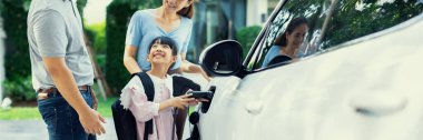 Progressive young happy family with electric vehicle and home backyard charging station. Green and clean energy from electric vehicles for healthy environment. Eco power from renewable source.