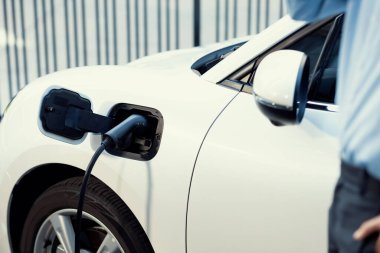 Arka planda bulanık bir işadamıyla şehrin kamu şarj istasyonundaki şarj bataryasına odaklan. Çevre dostu fikir için elektrikli şarjlı EV araba.