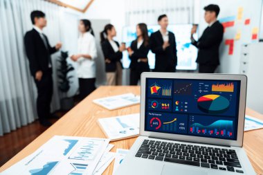 Focus laptop monitor display dashboard report by business intelligence, analyzed financial data for planning market strategy with blur background of standing office worker discussing in harmony office