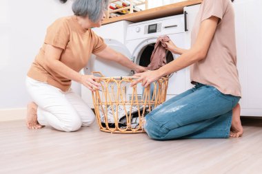 Daughter and mother working together to complete their household chores near the washing machine in a happy and contented manner. Mother and daughter doing the usual tasks in the house.