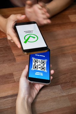 QR kodu parasız ödeme taraması için ekranda gösterilir. Kapalı eller, mobil uygulamadan elektronik işlem yoluyla para aktarmak için akıllı telefonu tutuyor. Hızlı ödeme için barkod teknolojisi. Coşkulu.