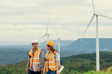 Erkek ve kadın mühendisler kırsal kesimdeki bir tepenin tepesinde ya da dağda rüzgar çiftliğinde çalışıyorlar. Yenilenebilir ve sürdürülebilir enerjinin gelecekteki üretimi için yenilikçi idealler.