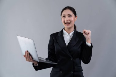 Kendine güvenen genç iş kadını izole edilmiş bir zeminde duruyor ve resmi siyah takım elbiseyle dizüstü bilgisayarda çalışıyor. Ofisteki kadın ya da yönetici, zeki ve profesyonel görünümlü. Coşkulu.