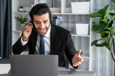 Erkek çağrı merkezi operatörü ya da telesales temsilcisi ofis masasında otururken kulaklık takıyor ve müşteri desteği sağlayan ya da ikna edici satış yapan müşteriyle sohbet ediyor. coşkulu