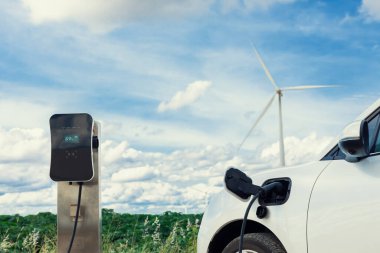 Progressive combination of wind turbine and EV car, future energy infrastructure. Electric vehicle being charged at charging station powered by renewable energy from wind turbine in the countryside.