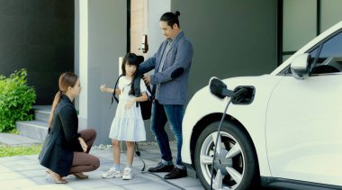 Progressive young parents and daughter with electric vehicle and home charging station. Green and clean energy from electric vehicles for healthy environment. Eco power from renewable source at home.