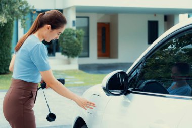 Progressive woman install cable plug to her electric car with home charging station. Concept of the use of electric vehicles in a progressive lifestyle contributes to clean environment.