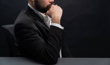 Resmi siyah takım elbiseli bir iş adamı ya da avukat izole edilmiş siyah arka planda oturuyor. Otorite ve ciddi jestleri olan bir adam kavramı. denge