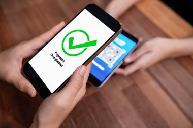 QR kodu parasız ödeme taraması için ekranda gösterilir. Kapalı eller, mobil uygulamadan elektronik işlem yoluyla para aktarmak için akıllı telefonu tutuyor. Hızlı ödeme için barkod teknolojisi. Coşkulu.