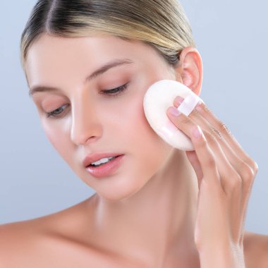 Closeup alluring beautiful female model applying powder puff for facial makeup concept. Portrait of flawless perfect cosmetic skin woman put powder foundation on her face in isolated background.