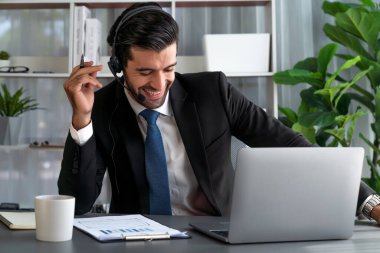 Erkek çağrı merkezi operatörü ya da telesales temsilcisi ofis masasında otururken kulaklık takıyor ve müşteri desteği sağlayan ya da ikna edici satış yapan müşteriyle sohbet ediyor. coşkulu