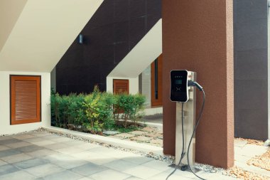 Progressive green energy-powered charging station concept for electric vehicle connected to home charging station at the garage or backyard. Eco friendly rechargeable car powered by clean energy.