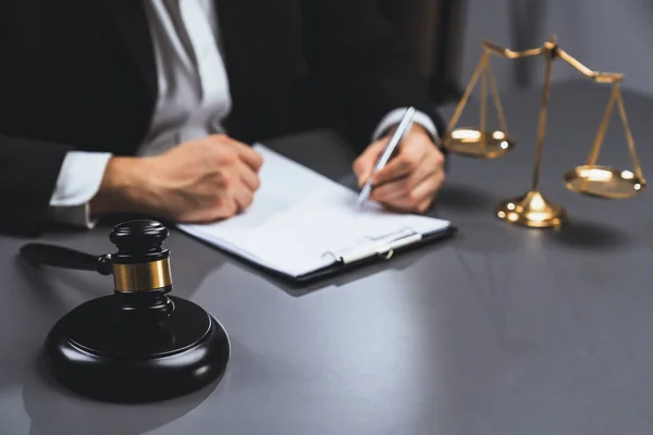 Focus symbols of justice, gavel hammer and scale balance on blurred background of lawyer or judge signing legal document at his desk for integrity and fairness of the legal system. equility