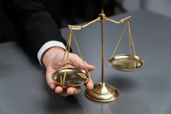 Lawyer in a black suit sits attentively on his office desk with a golden scale balance, symbol of legal justice and integrity, balanced and ethical decision making in the court of law. equility