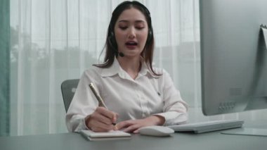 Masasında dizüstü bilgisayarla çalışan kulaklık ve mikrofon takan Asyalı müşteri destek operatörü. Hevesli kadın çalışanlar müşteri hizmetleri sunuyor, destekleyici çağrı merkezi temsilcisi müşterilere yardım ediyor.