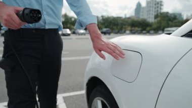 İlerici işadamı, şehir merkezinde dolaşmadan önce şarj cihazından elektrikli arabasına şarj prizi takıyor. Çevre dostu şarj edilebilir araba, sürdürülebilir ve temiz enerjiyle çalışıyor..