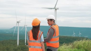 Erkek ve kadın mühendisler kırsal kesimdeki bir tepenin tepesinde ya da dağda rüzgar çiftliğinde çalışıyorlar. Yenilenebilir ve sürdürülebilir enerjinin gelecekteki üretimi için yenilikçi idealler.