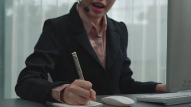 Masasında dizüstü bilgisayarla çalışan kulaklık ve mikrofon takan Asyalı müşteri destek operatörü. Hevesli kadın çalışanlar müşteri hizmetleri sunuyor, destekleyici çağrı merkezi temsilcisi müşterilere yardım ediyor.