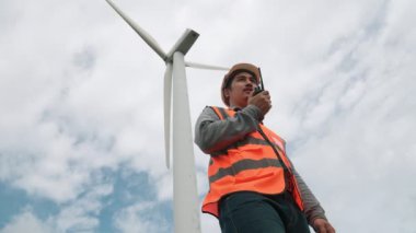 Gökyüzü arka planına sahip bir rüzgar türbini üzerinde çalışan mühendis. Yenilenebilir ve sürdürülebilir enerjinin gelecekteki üretimi için yenilikçi bir ideal. Rüzgar türbininden enerji üretimi.