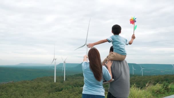 風力タービン農場で彼らの時間を楽しんで進歩的な幸せな家族の概念 水平線に丘や山を持つ国側の風力発電機による風力発電機 — ストック動画
