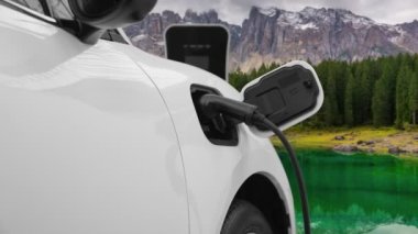 Temiz çevre için temiz enerjinin yol açtığı ilerici elektrikli araba kavramının arka planı olarak dağın tepesinde bulutun zaman kavramının yer aldığı doğal manzara. EV araba şarj istasyonunda şarj oluyor..
