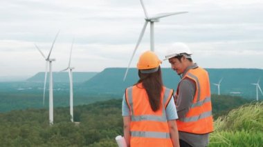 Erkek ve kadın mühendisler kırsal kesimdeki bir tepenin tepesinde ya da dağda rüzgar çiftliğinde çalışıyorlar. Yenilenebilir ve sürdürülebilir enerjinin gelecekteki üretimi için yenilikçi idealler.