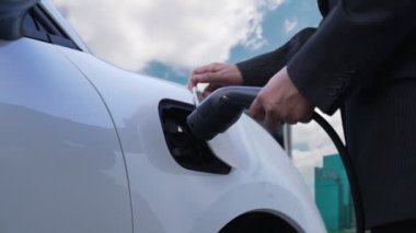 Elektrikli araç, iş adamı yüksek gökdelenlerle çevrili kentsel alandaki şarj istasyonunda EV akü şarj ediyor. Çevre dostu yenilikçi temiz enerji kavramı.