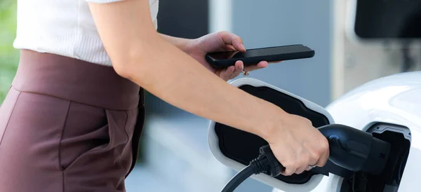 Stock image Closeup progressive woman install cable plug to her electric car with home charging station. Concept of the use of electric vehicles in a progressive lifestyle contributes to clean environment.