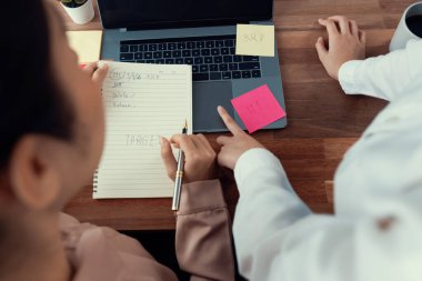 Modern ofis çalışma alanında iş birliği yapan iki ofis çalışanı, tartışmalar ve dizüstü bilgisayarla birlikte çalışma, profesyonel ve modern ofis çalışanı olarak not yazma. Coşkulu.