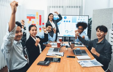 İş adamları TV ekranında başarılı bir sunum veya veri analizi toplantısından sonra kutlama yapıyorlar. Mutlu takım ofis odasında toplanıyor, kutlama jestleriyle işbirliği için tezahürat yapıyorlar. Uyum